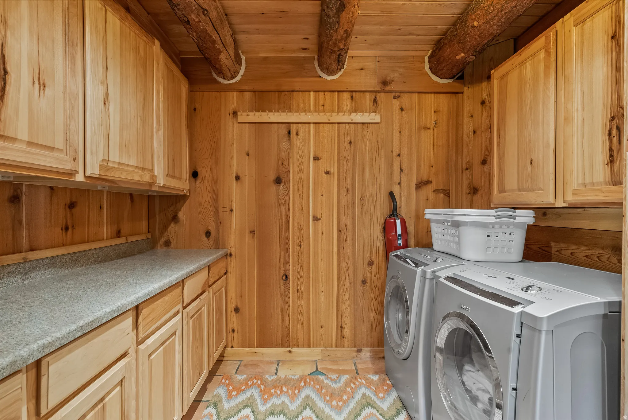 Utility room featuring wood plank walls, wood beam ceiling, wood cabinetry, a light-toned countertop, and tile flooring
