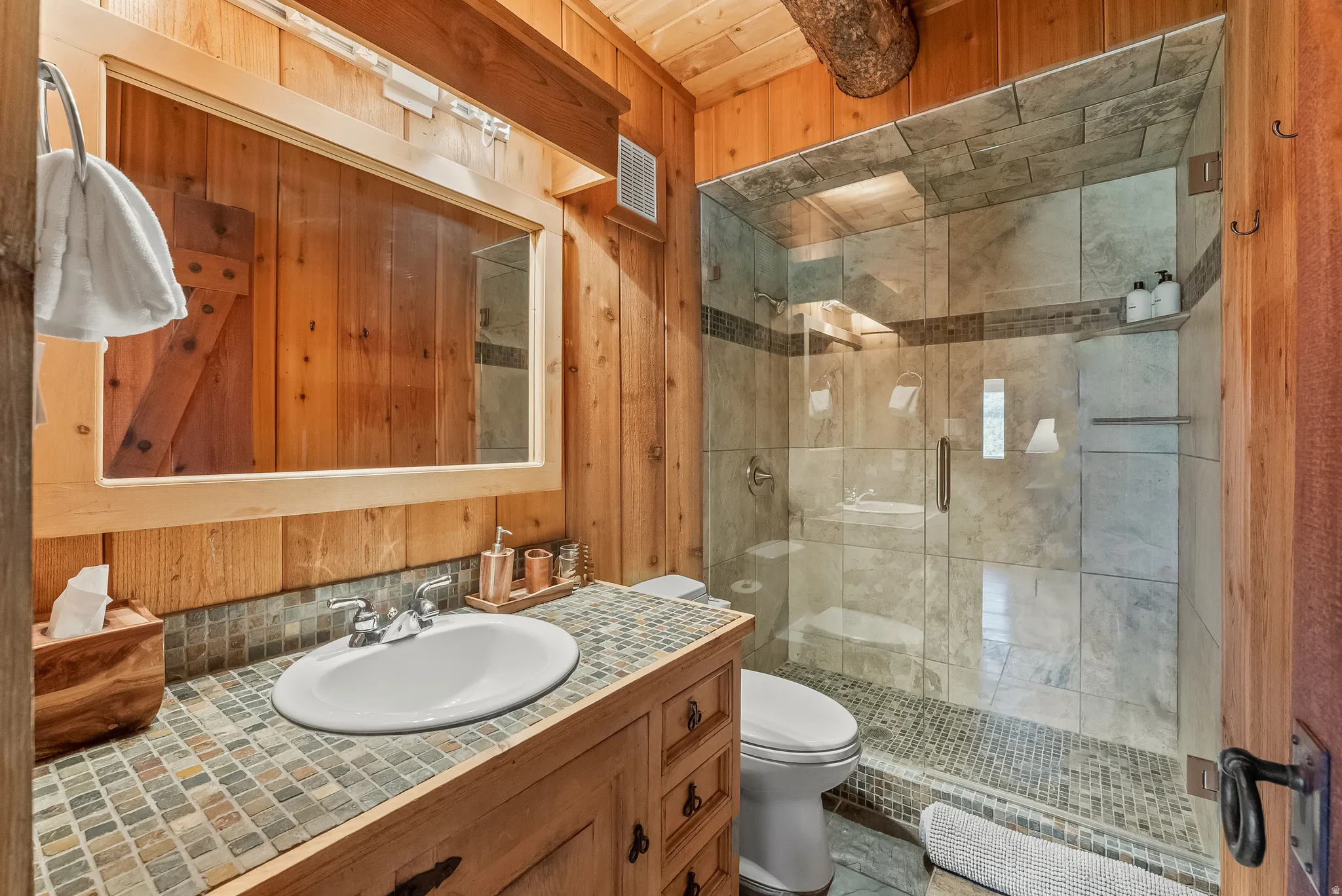 Wood-paneled bathroom featuring a glass-enclosed shower with tile surround and stone flooring