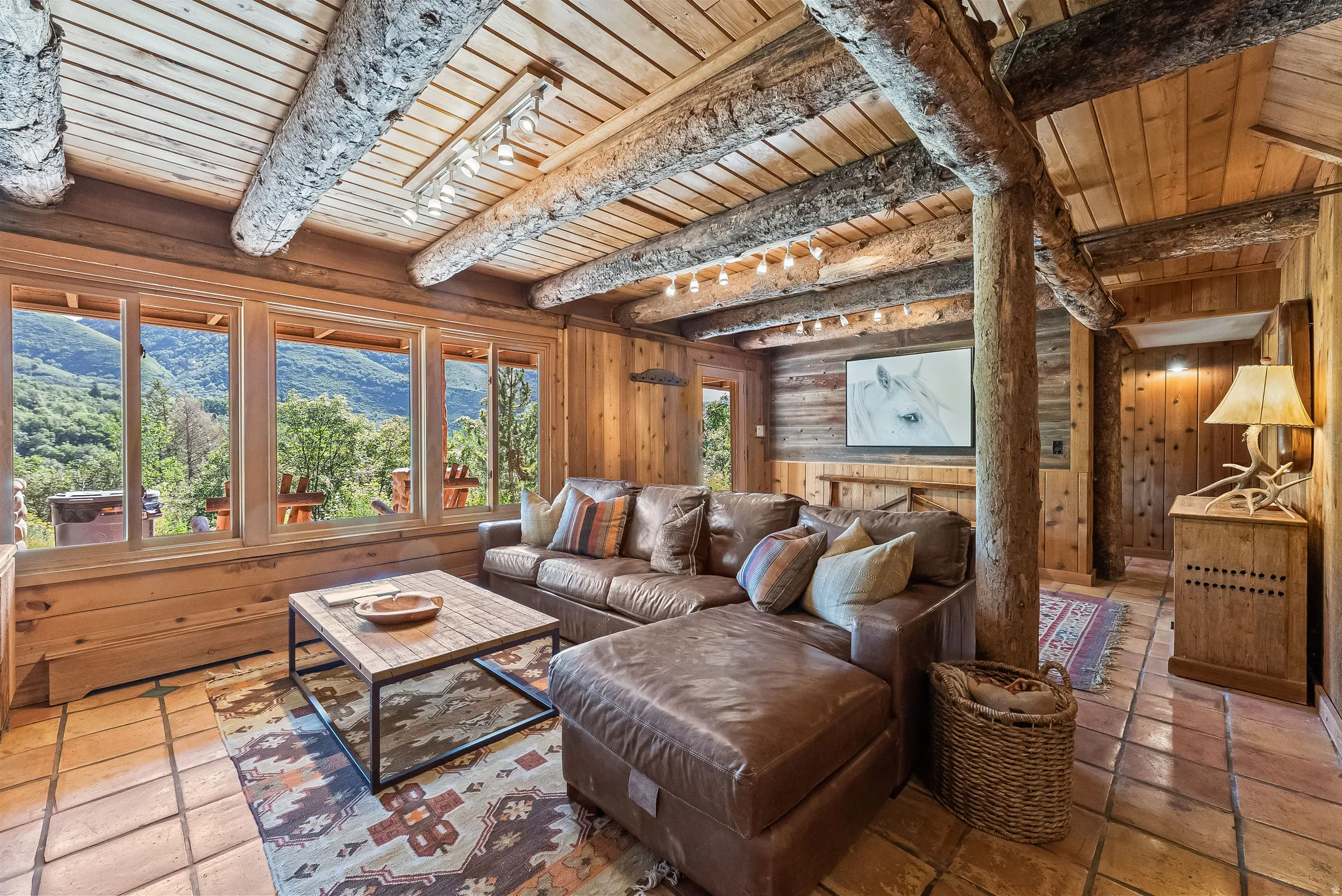 Rustic living area featuring exposed log beams, wood plank ceilings, and paneled walls