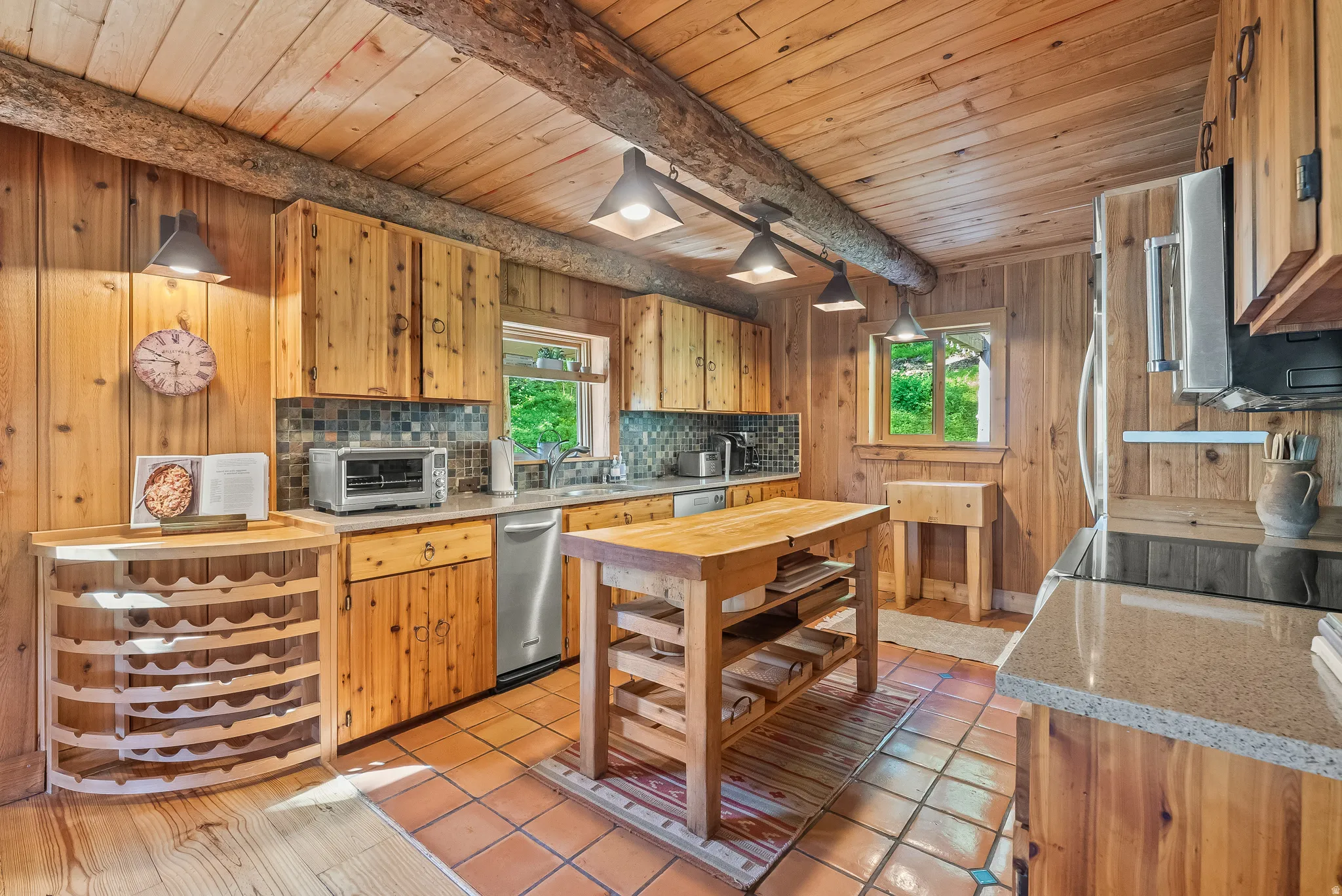 Kitchen featuring wood-paneled walls and ceiling, exposed log beams, and terracotta tile flooring