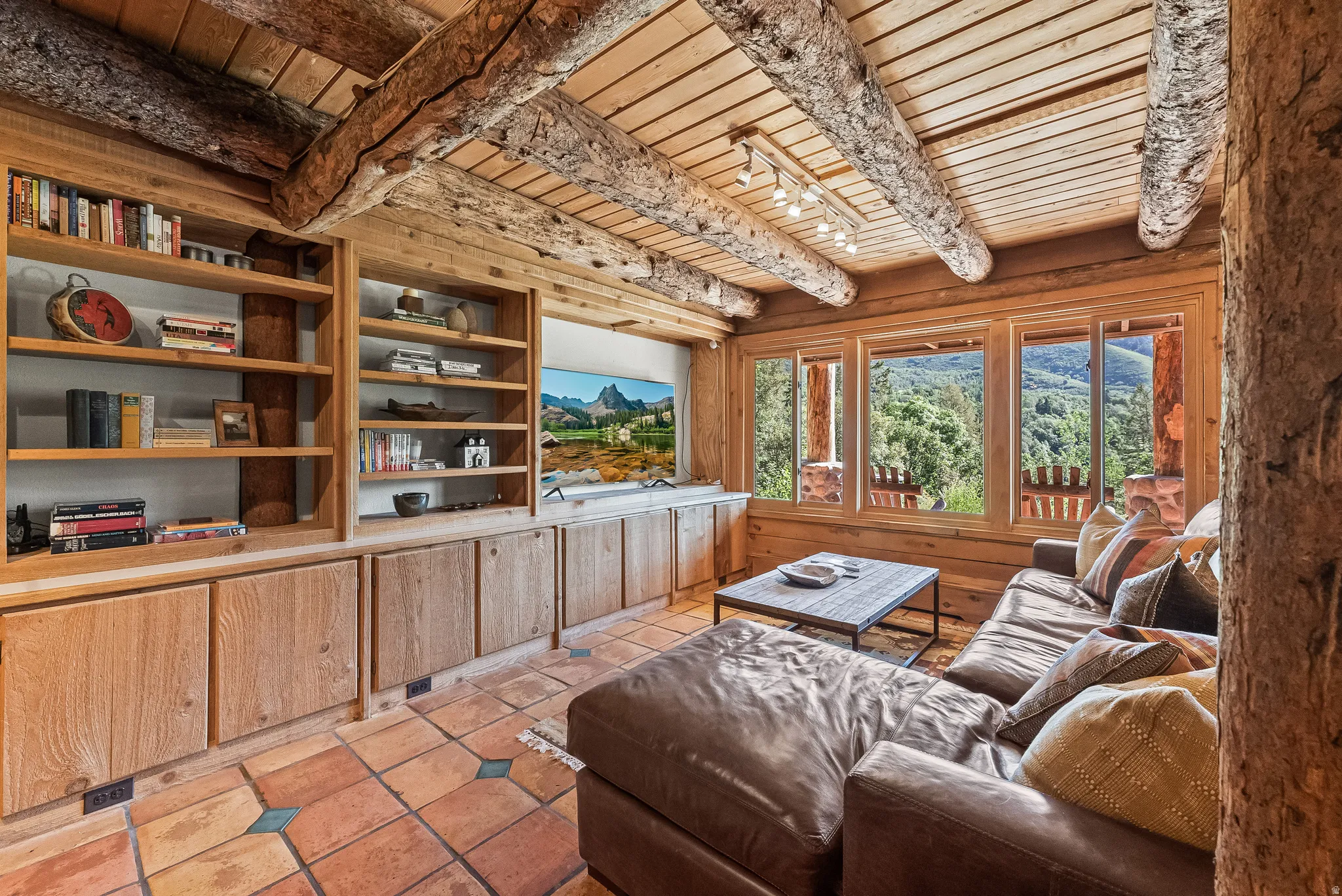 Rustic living area featuring exposed log beams, wood-planked ceilings, and a built-in entertainment center with open shelving and cabinet storage