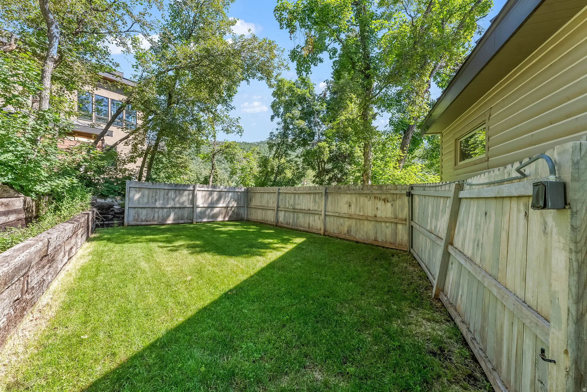 Private backyard featuring a manicured lawn, full perimeter wood fencing, and a built-in timber retaining wall