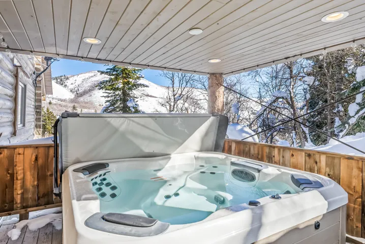 Covered outdoor hot tub with mountain scenery, log cabin exterior, wood-finish railing, and recessed ceiling lighting