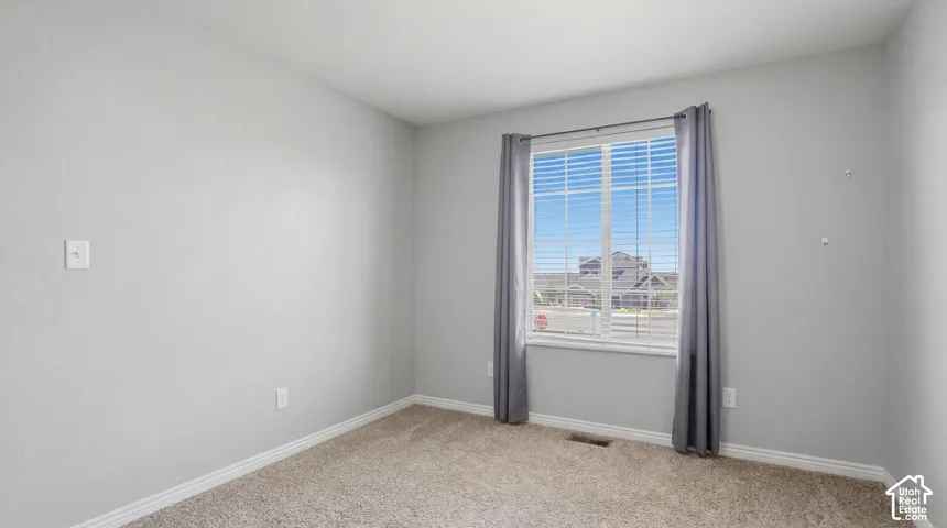 Carpeted room featuring a single window with blinds and drapes, light gray wall paint, and white baseboards