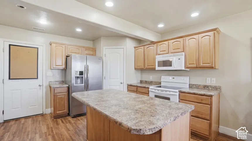 Kitchen featuring a central island with a stone-finish countertop, wood-finish flooring, light wood cabinetry, and stainless steel appliances