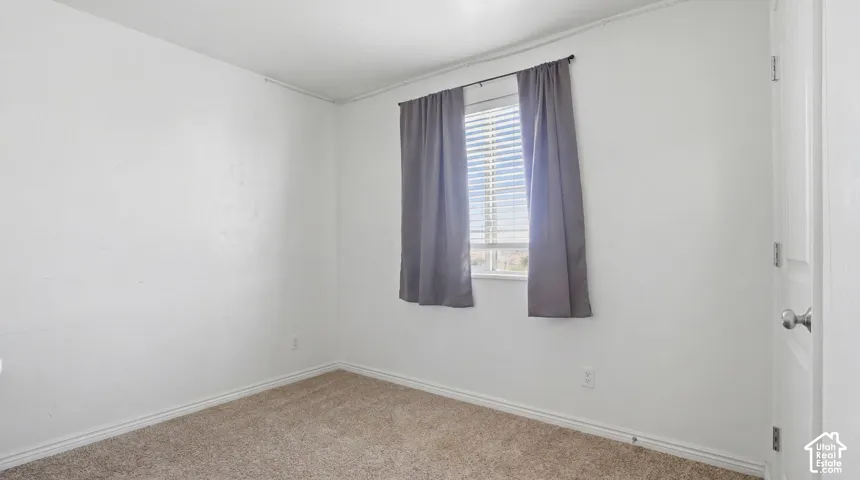 Spacious room featuring neutral carpeting, white walls, and a window with blinds and drapes