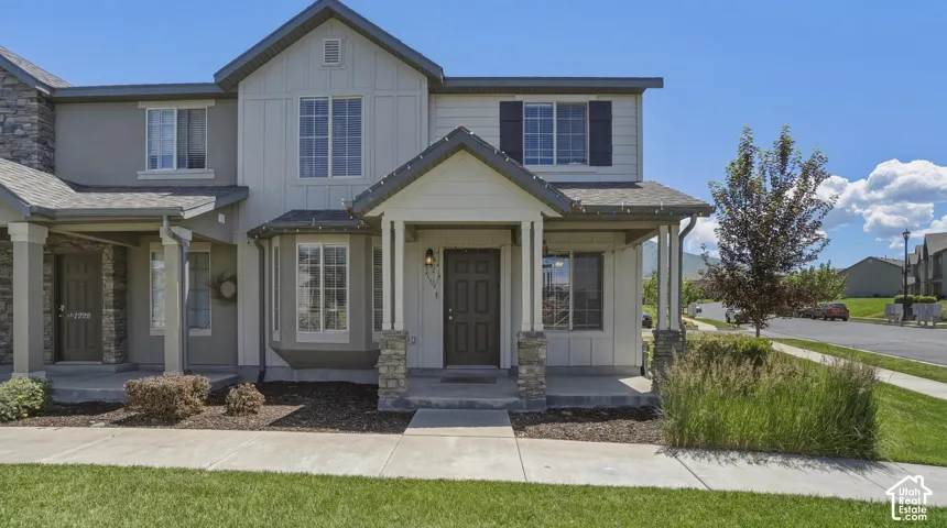 Modern townhome exterior featuring a covered porch with stone-clad columns, dark entry door, and a combination of vertical and horizontal siding