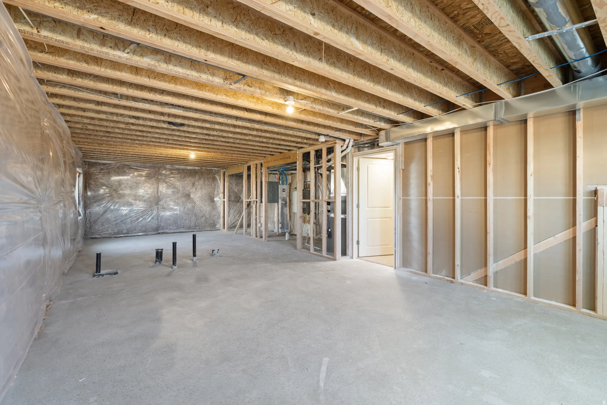 Unfinished lower level featuring exposed wood joists, concrete flooring, framed interior walls, visible plumbing rough-ins, and a pre-hung interior door