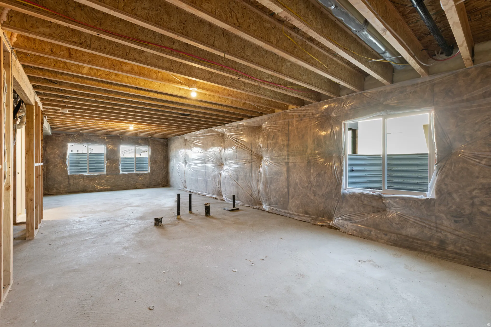 Unfinished basement featuring exposed wood joists, concrete flooring, and multiple windows