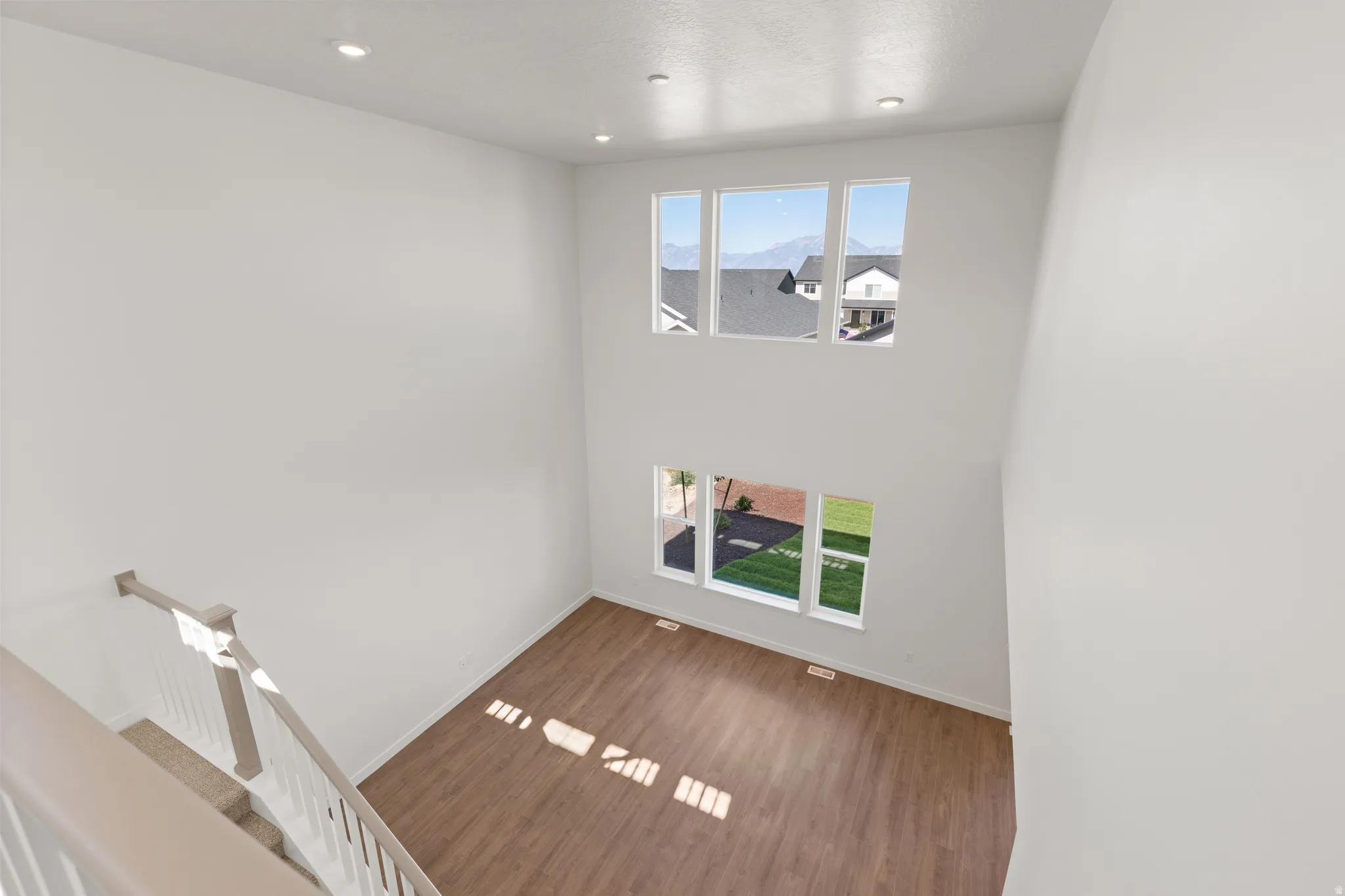 Two-story great room featuring high ceilings, multiple windows, recessed lighting, wood-finish flooring, and a carpeted staircase with white railings