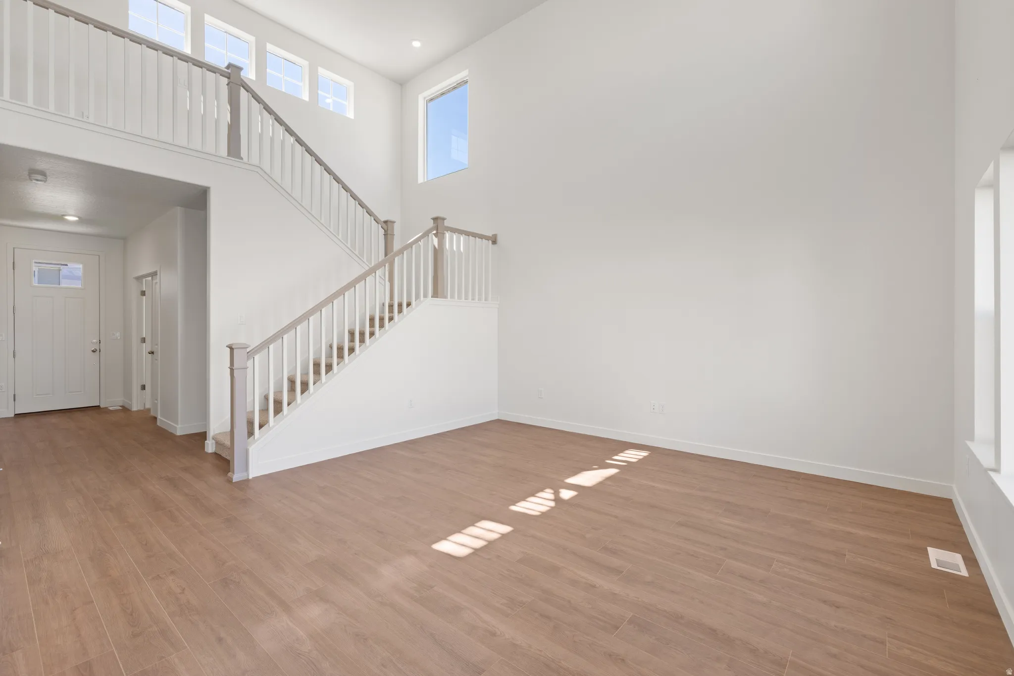 Two-story foyer featuring wood-finish flooring, a contemporary staircase with white balusters and light wood-tone handrails, and high ceilings