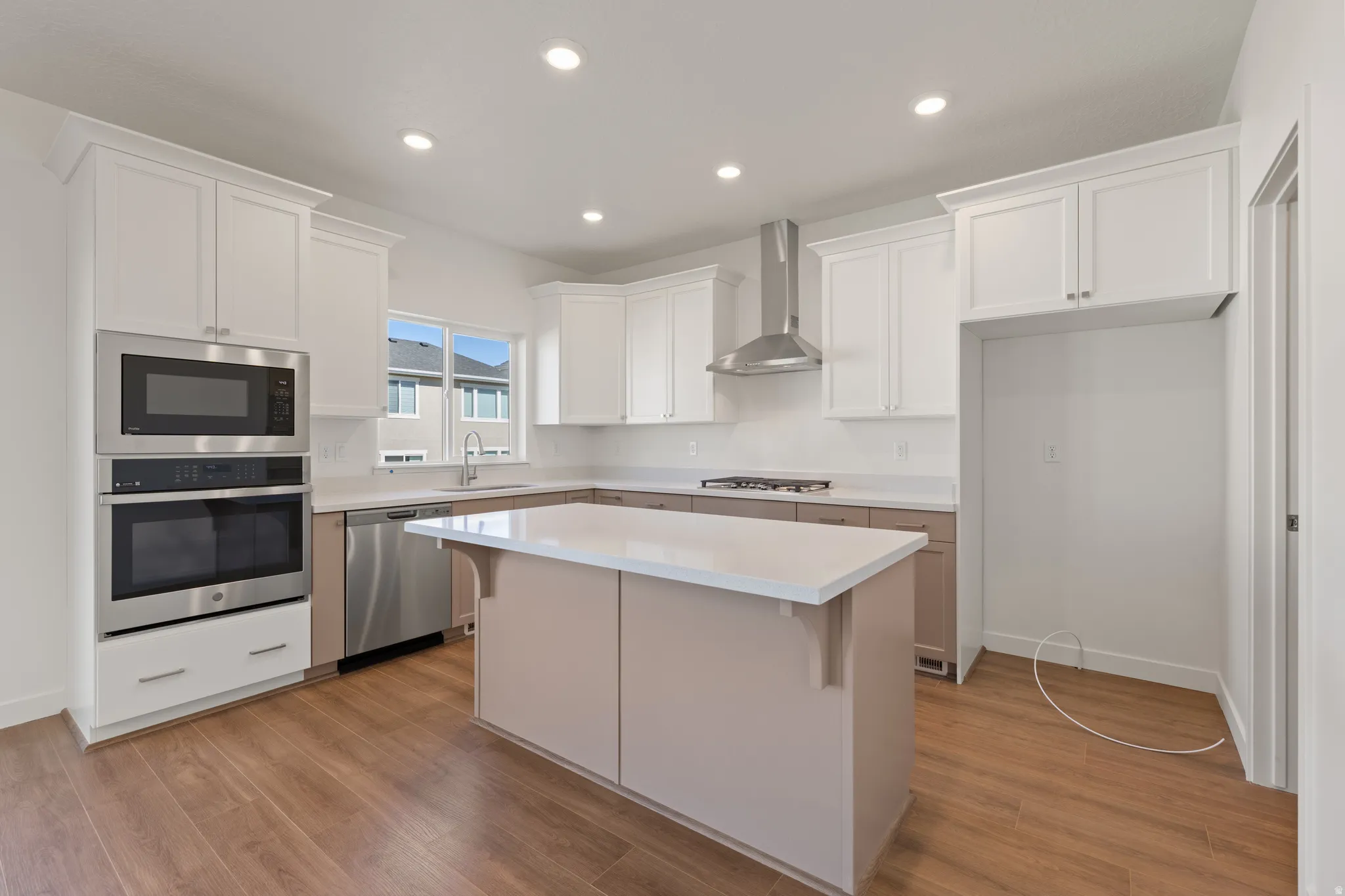 Bright kitchen featuring wood-finish flooring, white upper cabinetry, and a central island with a solid surface countertop