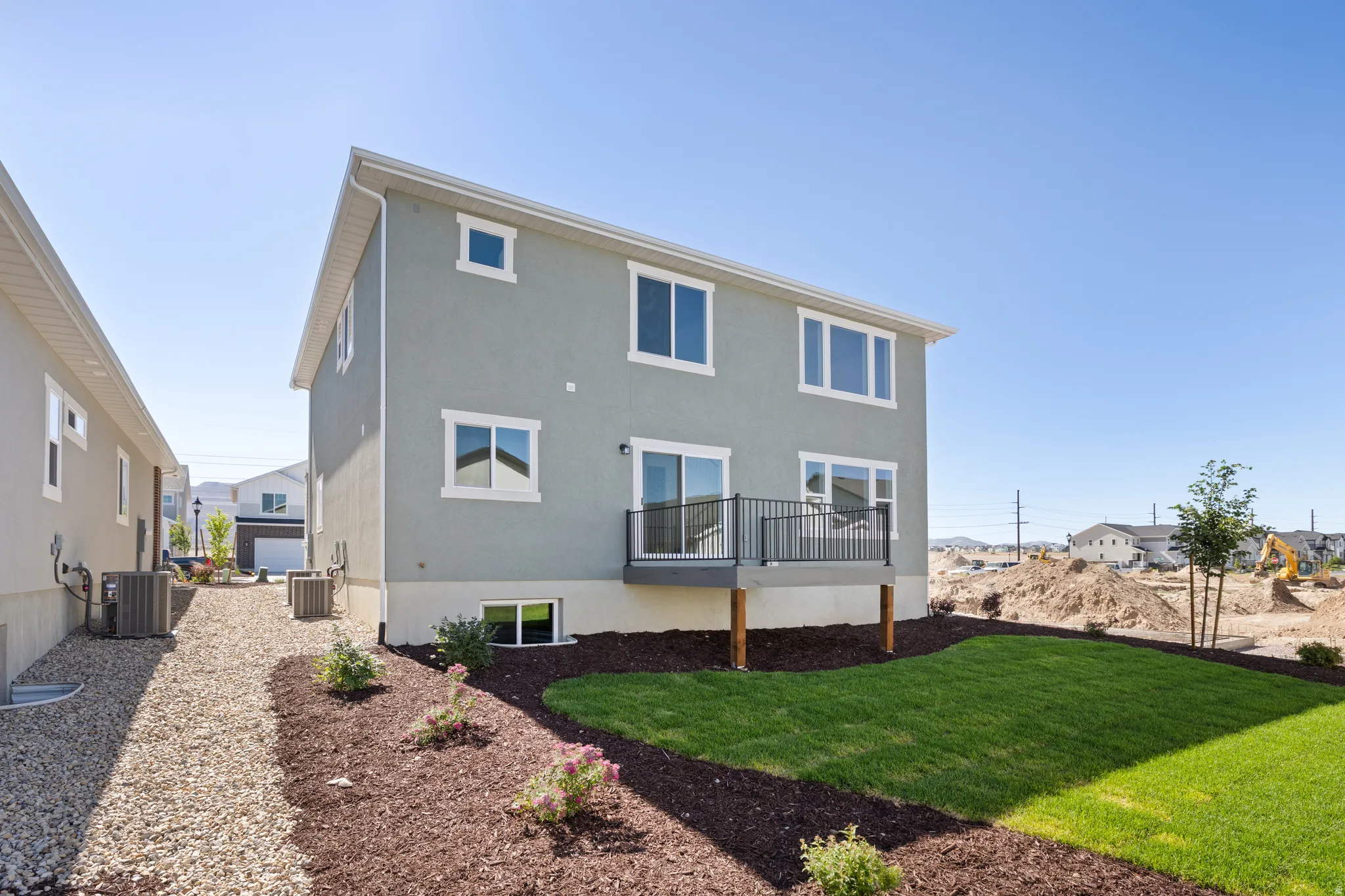 Expansive rear exterior featuring a raised deck with black metal railing, a manicured lawn area, and a gravel side path