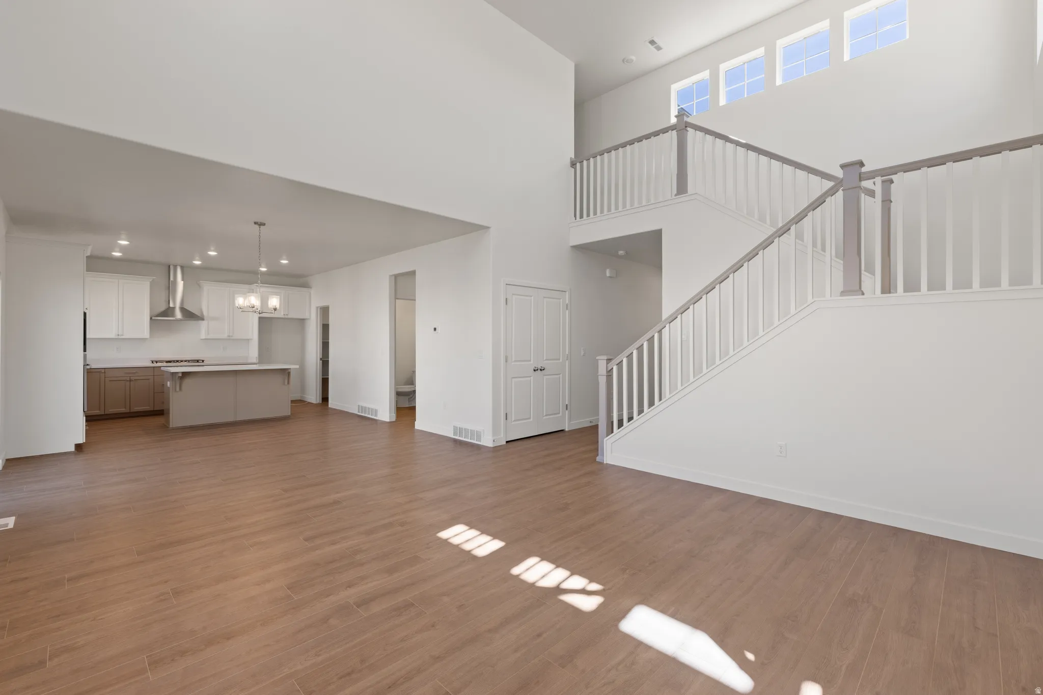 Open-concept living space featuring wood-finish flooring, a contemporary kitchen, and a double-height ceiling