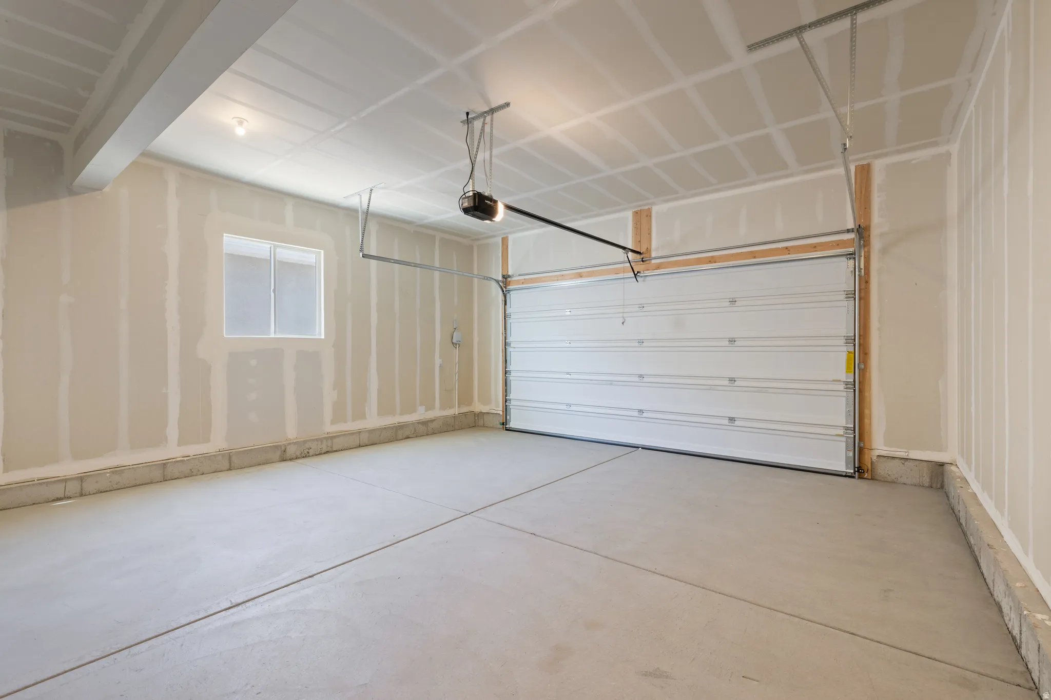 Spacious garage featuring concrete flooring, a white paneled garage door, exposed drywall, and a functional window
