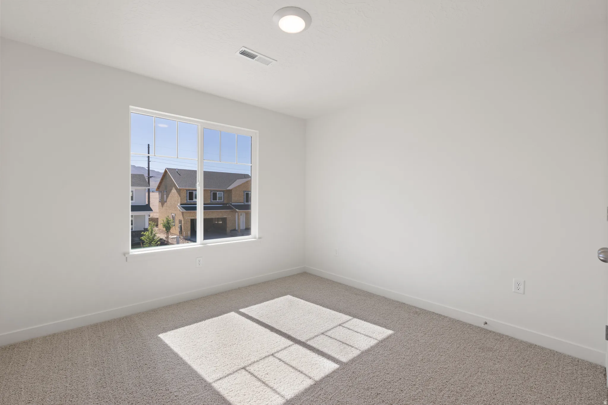 Bright room featuring a large window, plush carpeting, clean white walls, a flush-mount ceiling light, and white baseboards