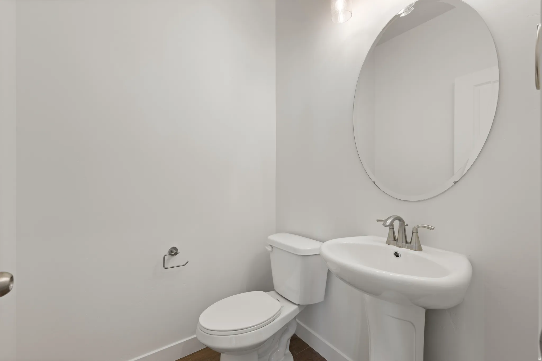 Pedestal sink with brushed nickel faucet, oval mirror, and overhead vanity lighting