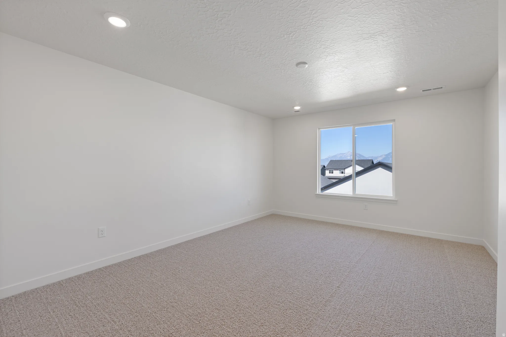 Spacious room with plush carpeting, recessed lighting, and a large window providing natural light