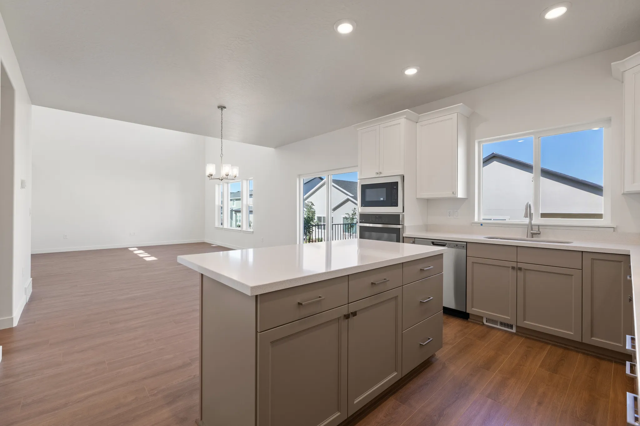 Kitchen featuring a central island with countertop, stainless steel appliances, upper white cabinetry, lower taupe cabinetry, and wood-finish flooring