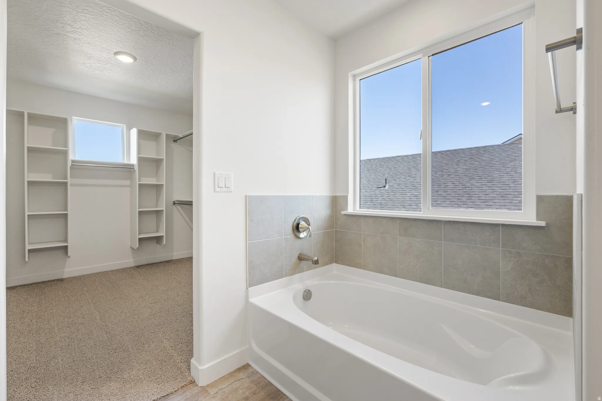 White soaking tub with grey tile surround and a large window