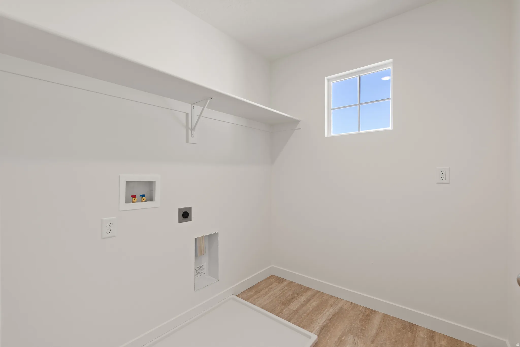 Utility space featuring a window, wood-finish flooring, a white shelf, and appliance hookups