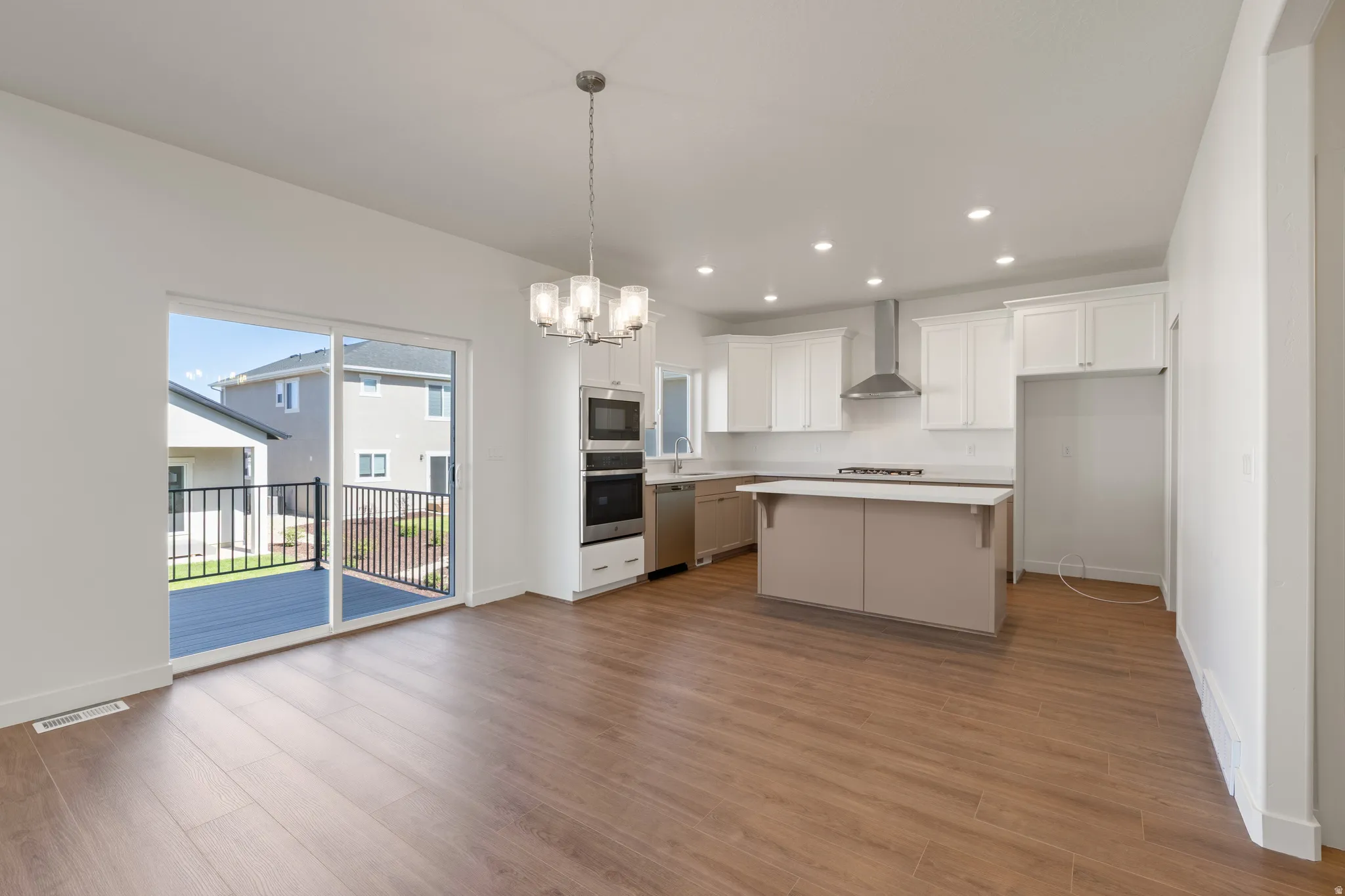 Open-concept kitchen and dining area featuring wood-finish flooring, white cabinetry, recessed lighting, and a stainless steel oven and microwave tower