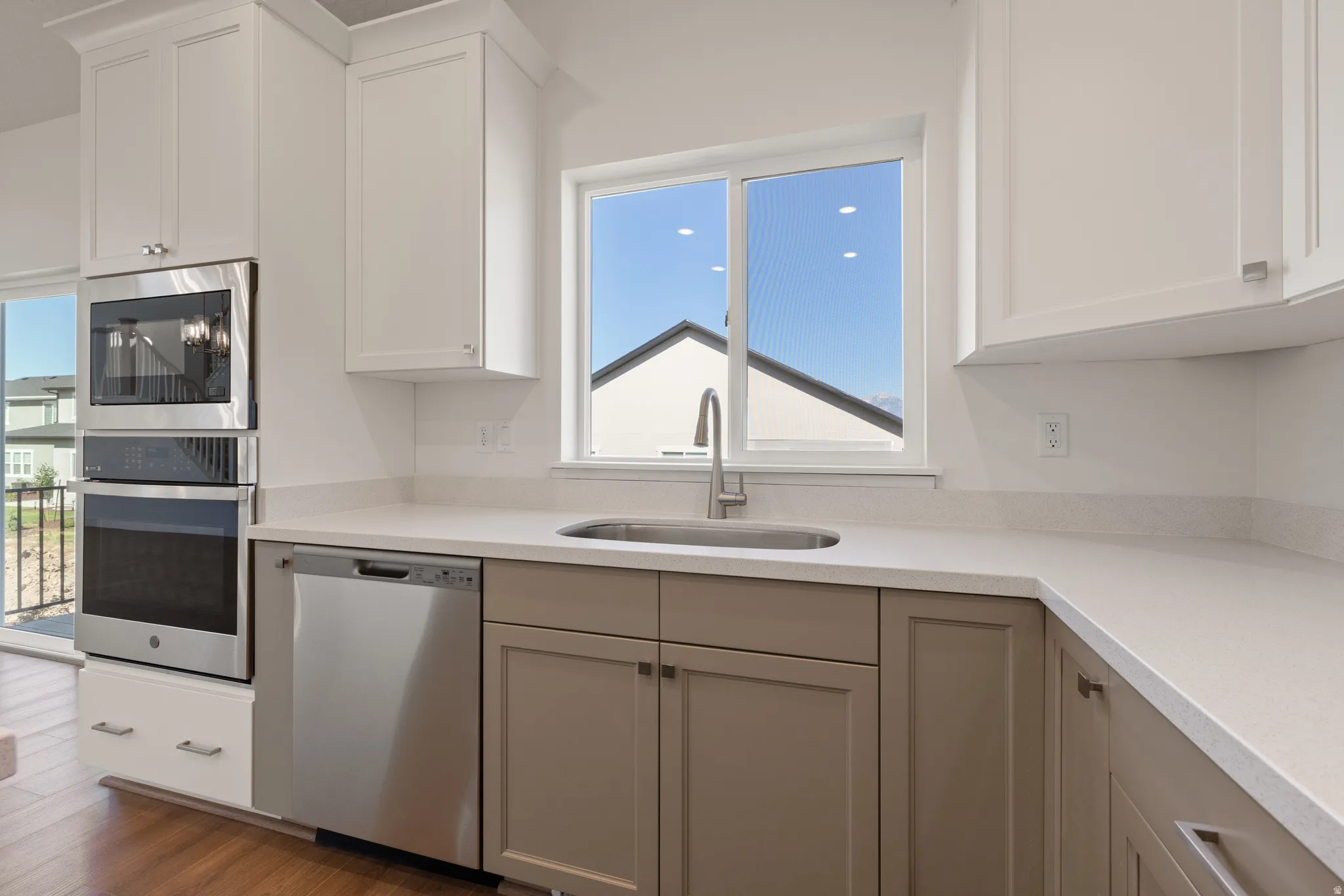Kitchen featuring white upper cabinetry, two-tone lower cabinetry, stainless steel appliances, a corner sink with a gooseneck faucet, and light-colored countertops