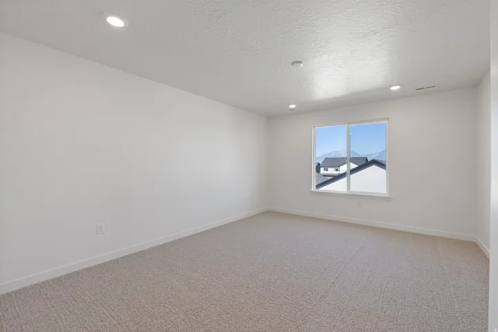 Spacious room with plush carpeting, recessed lighting, and a large window providing natural light