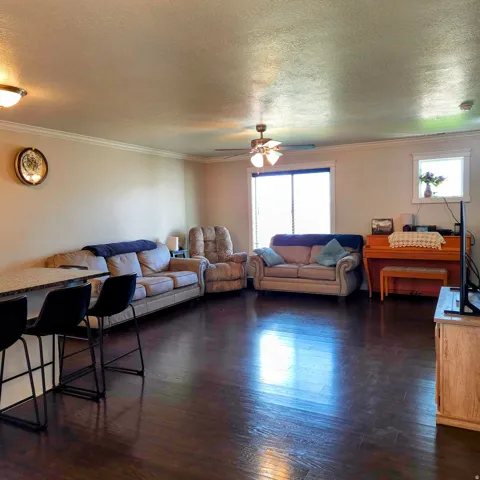 Spacious living area featuring dark wood-finish flooring, crown molding, and a ceiling fan with integrated lighting