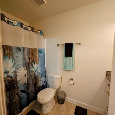 Bathroom featuring a shower-tub combination, a standard toilet, and tiled flooring