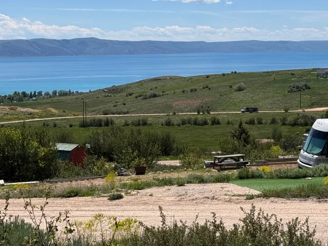 Expansive property featuring a red outbuilding, green cultivated patches, a gravel foreground, and distant water scenery