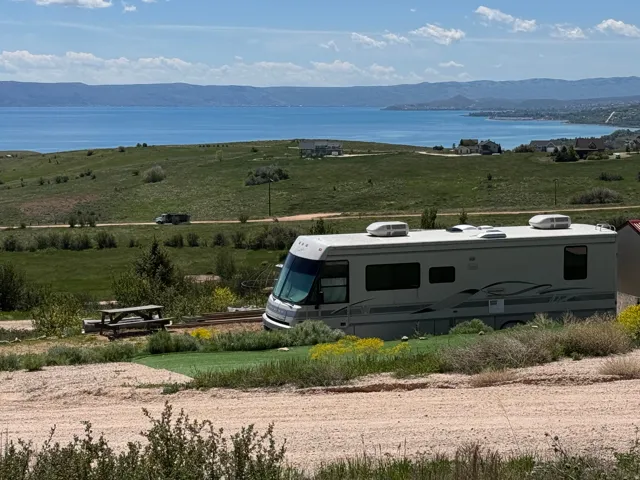 Expansive property featuring a picnic table, a gravel and grass-covered ground, and distant water scenery