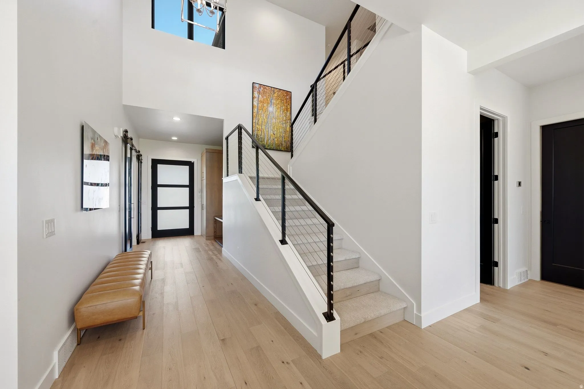 Two-story entryway featuring wood-finish flooring, a contemporary staircase with cable railing, a large window, a modern chandelier, and dark-paneled interior doors