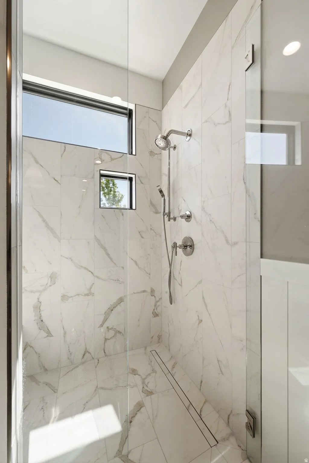 Walk-in shower featuring full-height porcelain tile, frameless glass enclosure, linear drain, transom window, and integrated niche