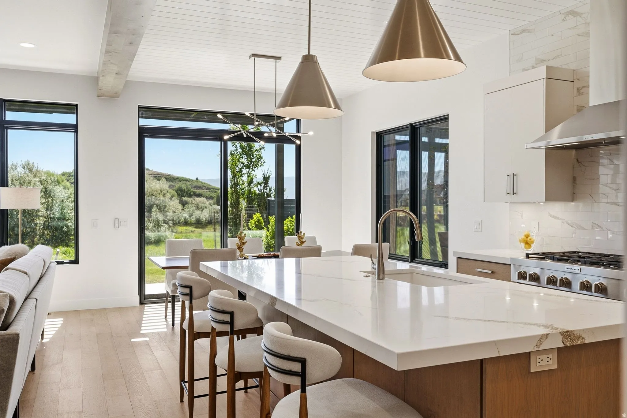 Open-concept kitchen and dining area featuring a waterfall island with an integrated sink, stainless steel appliances, and a tiled backsplash