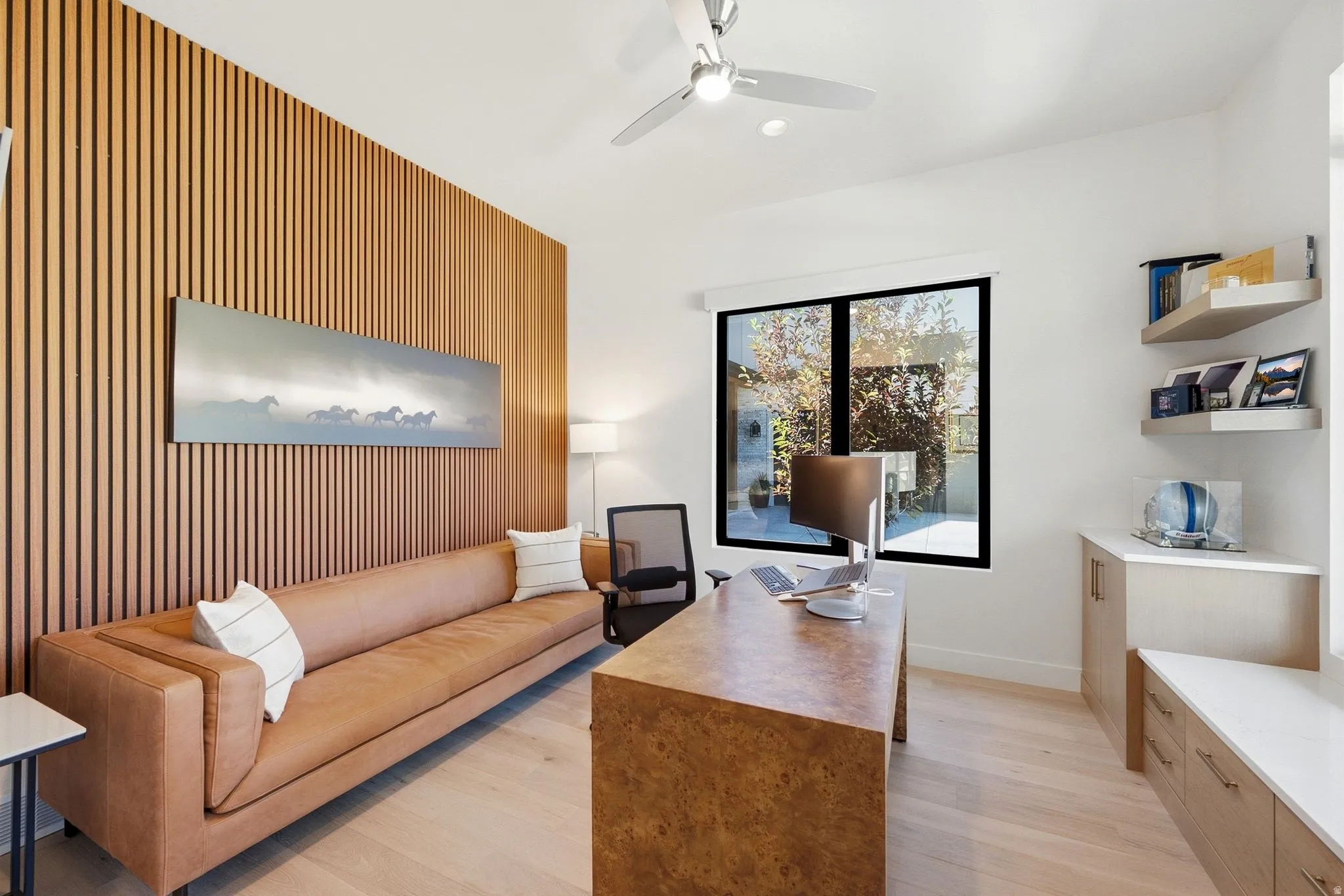 Bright room featuring a prominent wood-slat accent wall, light wood-finish flooring, and a large window providing outdoor illumination