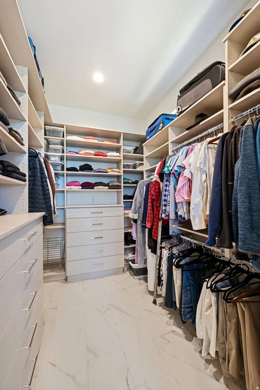 Custom walk-in closet featuring extensive built-in shelving, multiple hanging rods, integrated drawer units with metal pull handles, and recessed ceiling lighting