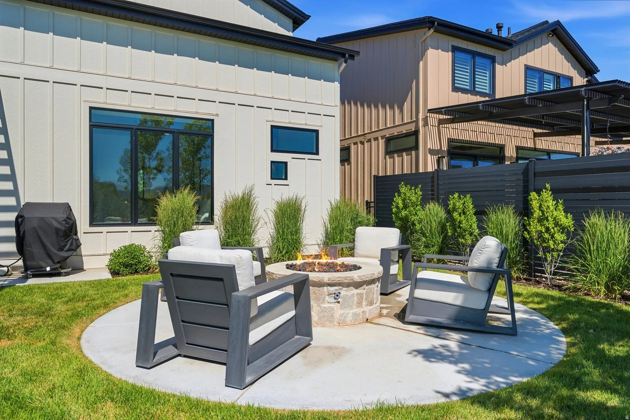 Private outdoor patio featuring a circular concrete pad, a stone fire pit, and a surrounding lawn