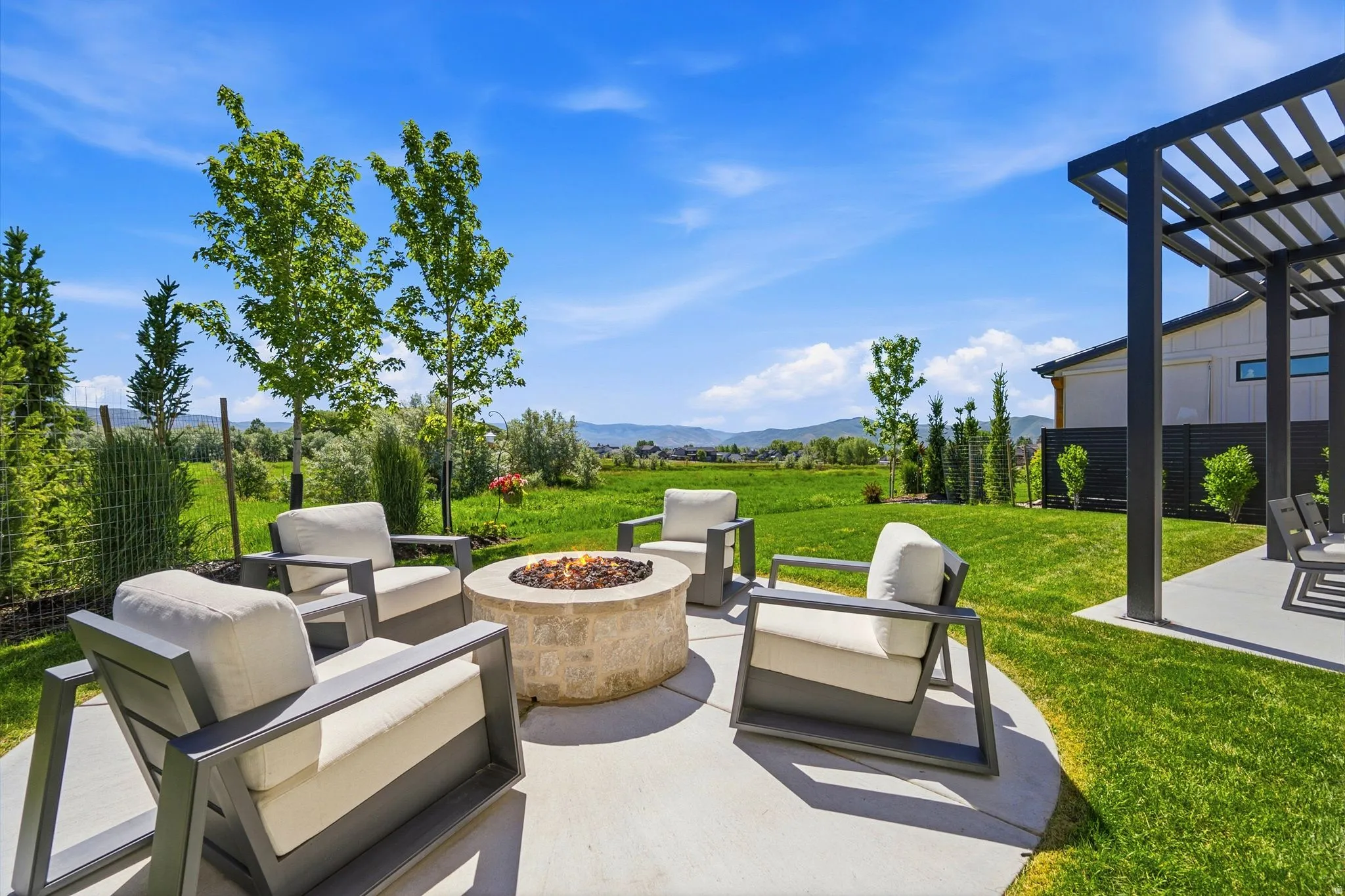Expansive backyard featuring a circular concrete patio with a built-in stone fire pit, a flat lawn, and a modern pergola