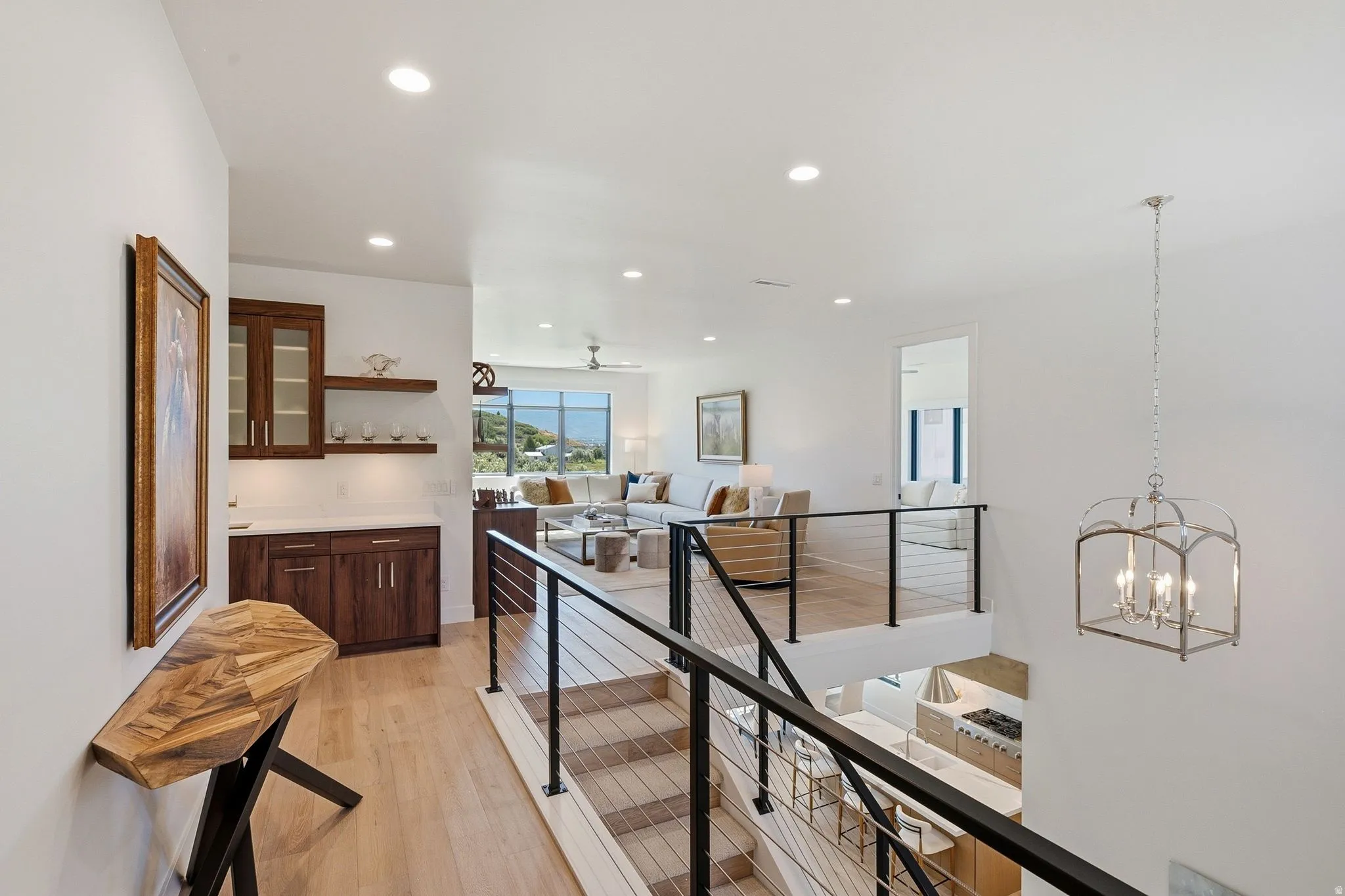 Staircase featuring cable railing and light wood-finish treads, complemented by a built-in wet bar with dark wood cabinetry and floating shelves