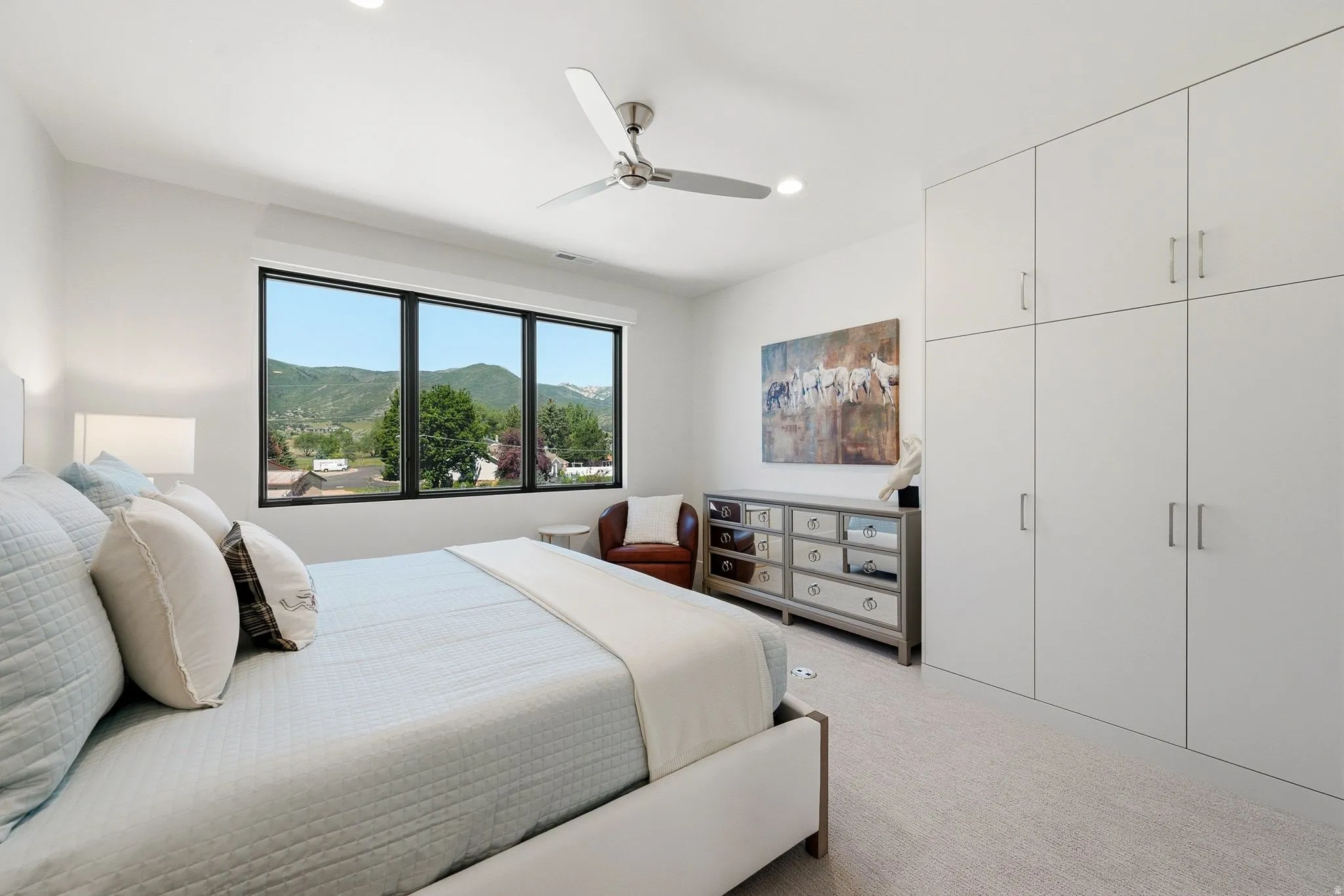 Bright bedroom with large multi-pane window, flush-mounted ceiling lighting, and a ceiling fan