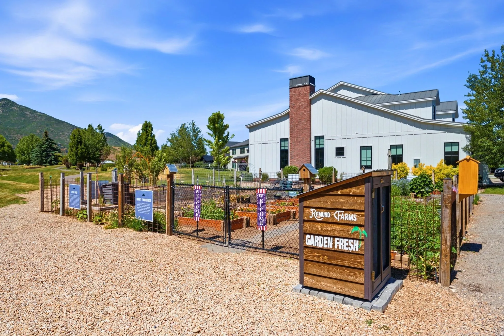 Community garden beds featuring mature plants, wood fencing, and a gravel pathway