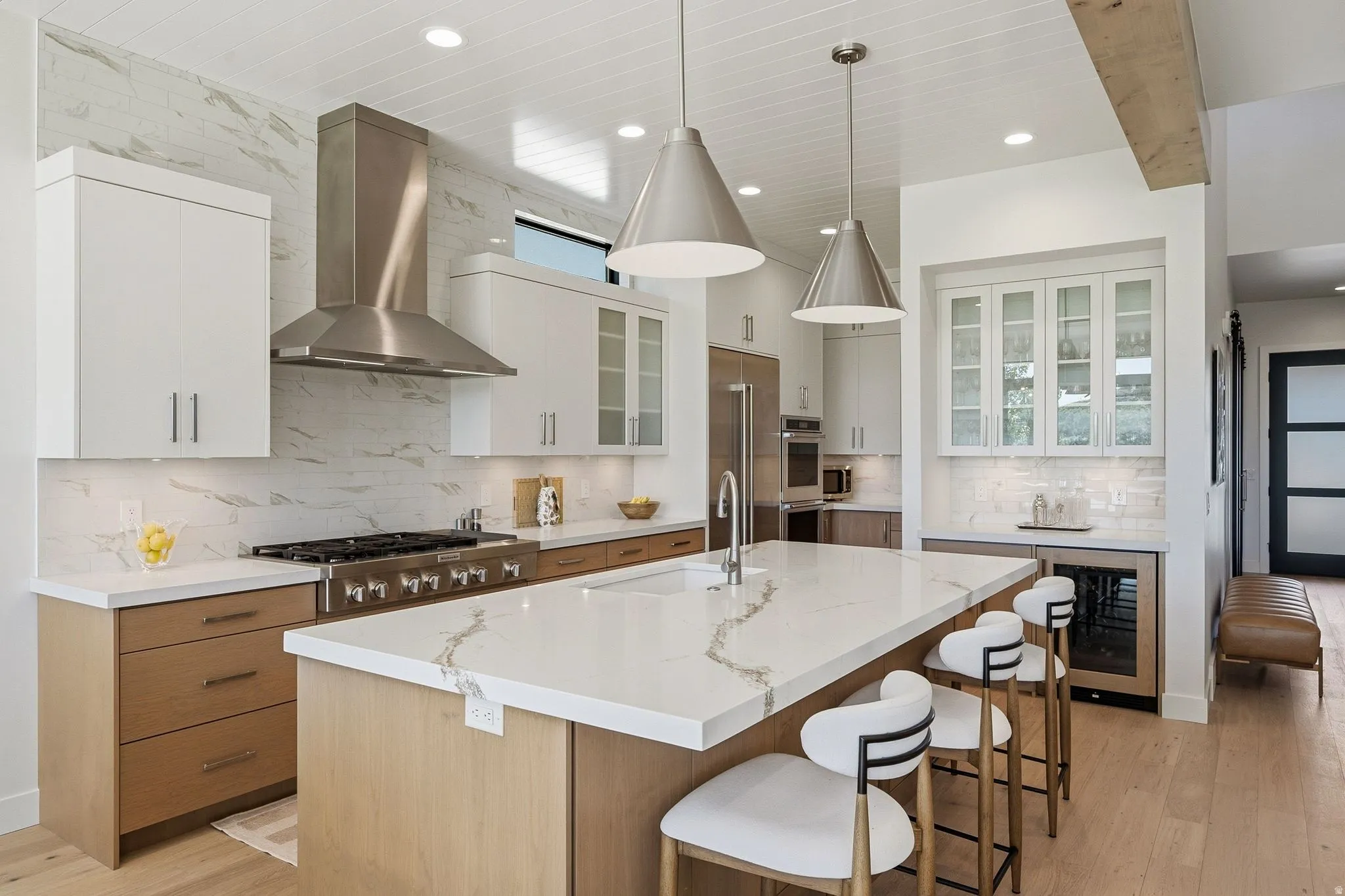 Gourmet kitchen featuring a large central island with seating, stainless steel appliances, white cabinetry, wood-finish lower cabinetry, and a textured backsplash