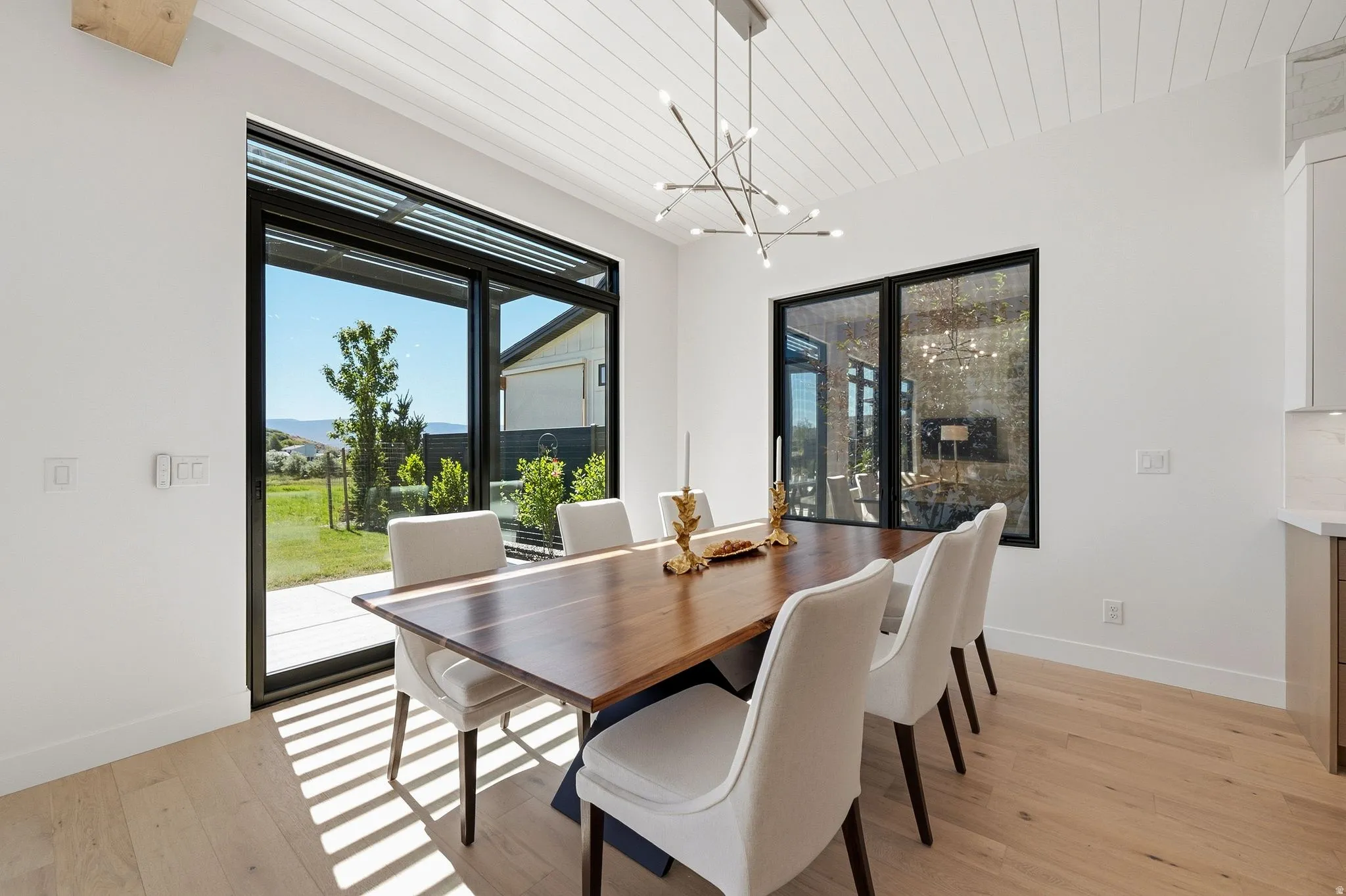 Dining area with a geometric chandelier, white plank ceiling, and light wood-finish flooring