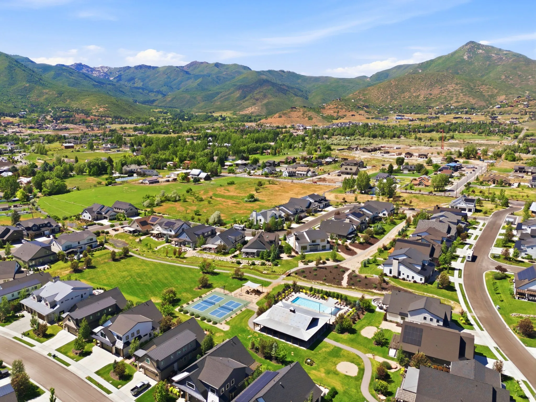 Expansive community featuring contemporary residential architecture, mountain backdrops, recreational courts, and a swimming pool facility