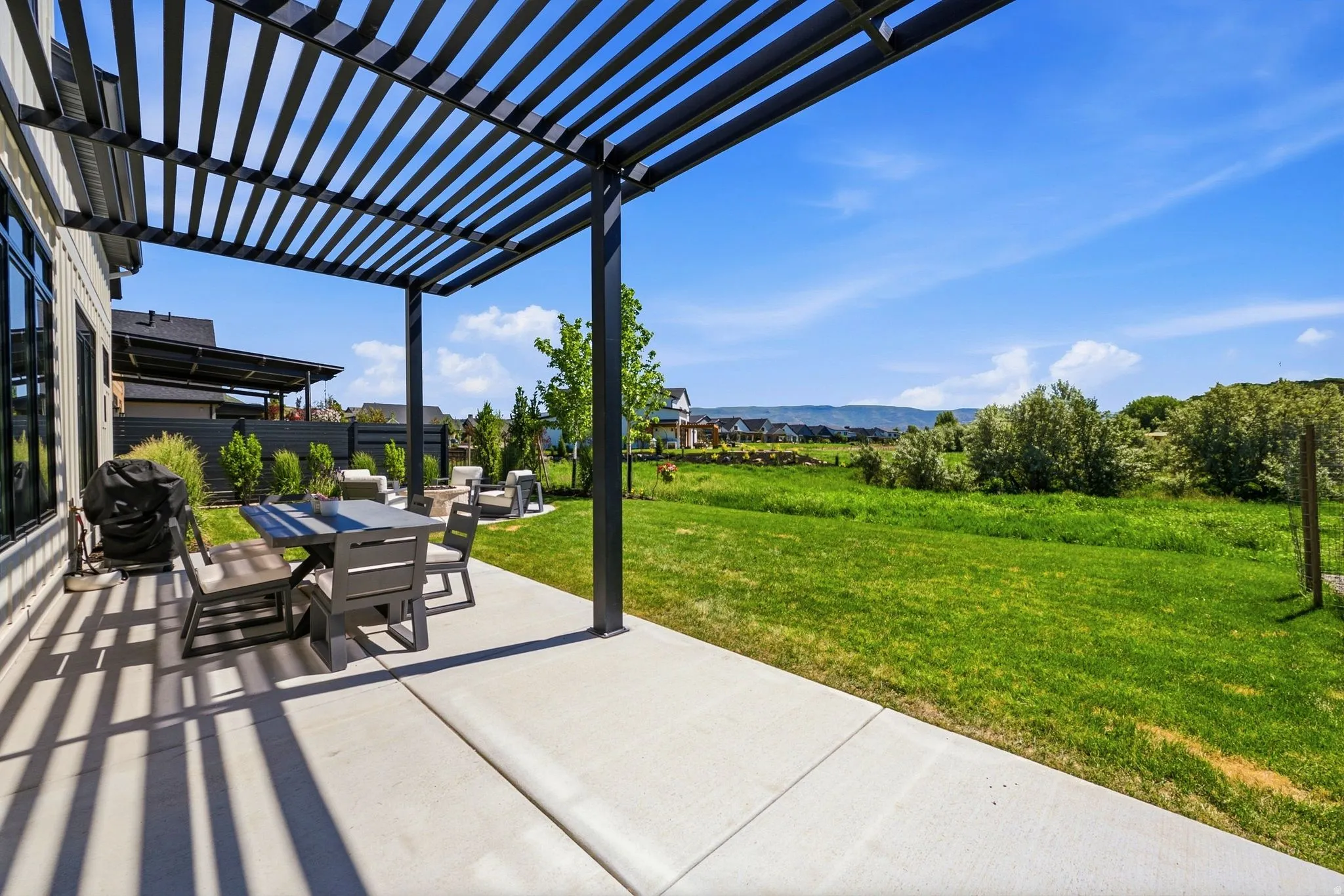 Expansive concrete patio with a modern black pergola and a substantial grassy area