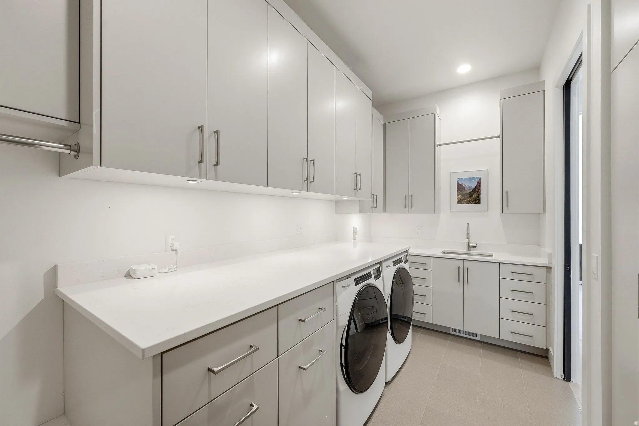 Modern laundry area featuring extensive overhead and base cabinetry, light-toned countertops, and a built-in sink with a gooseneck faucet