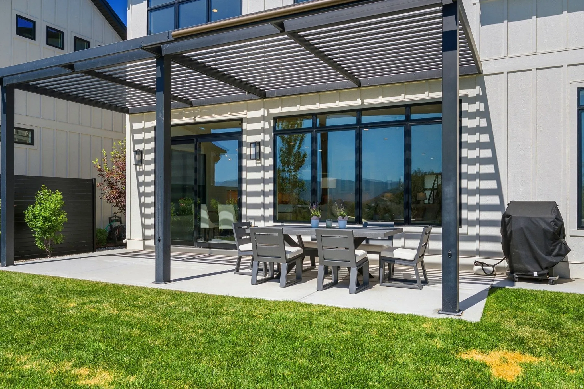 Exterior patio with a black slatted pergola over concrete surfacing