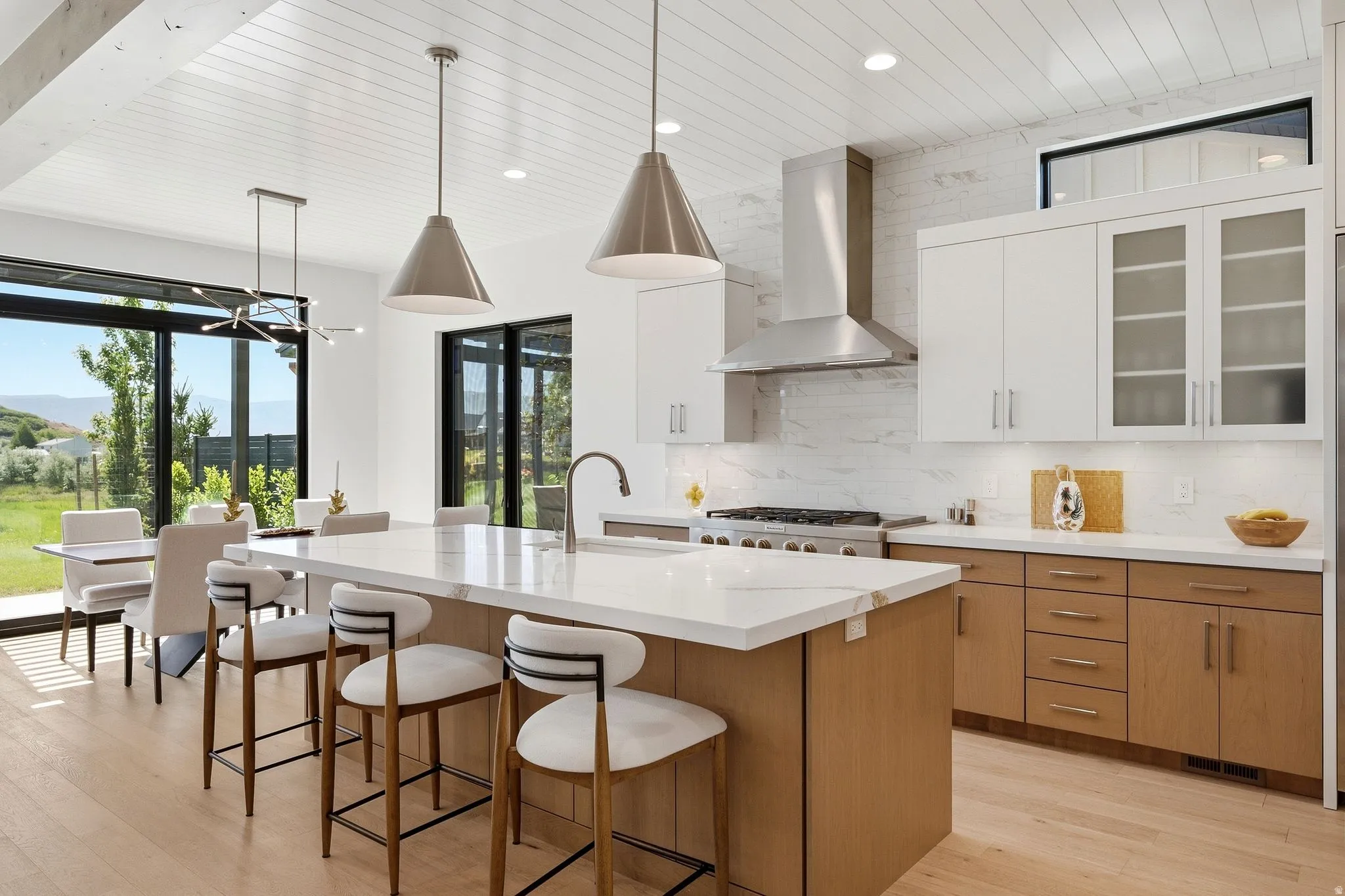 Modern kitchen featuring a large central island with seating, stainless steel appliances, a white tile backsplash, and light wood-finish flooring