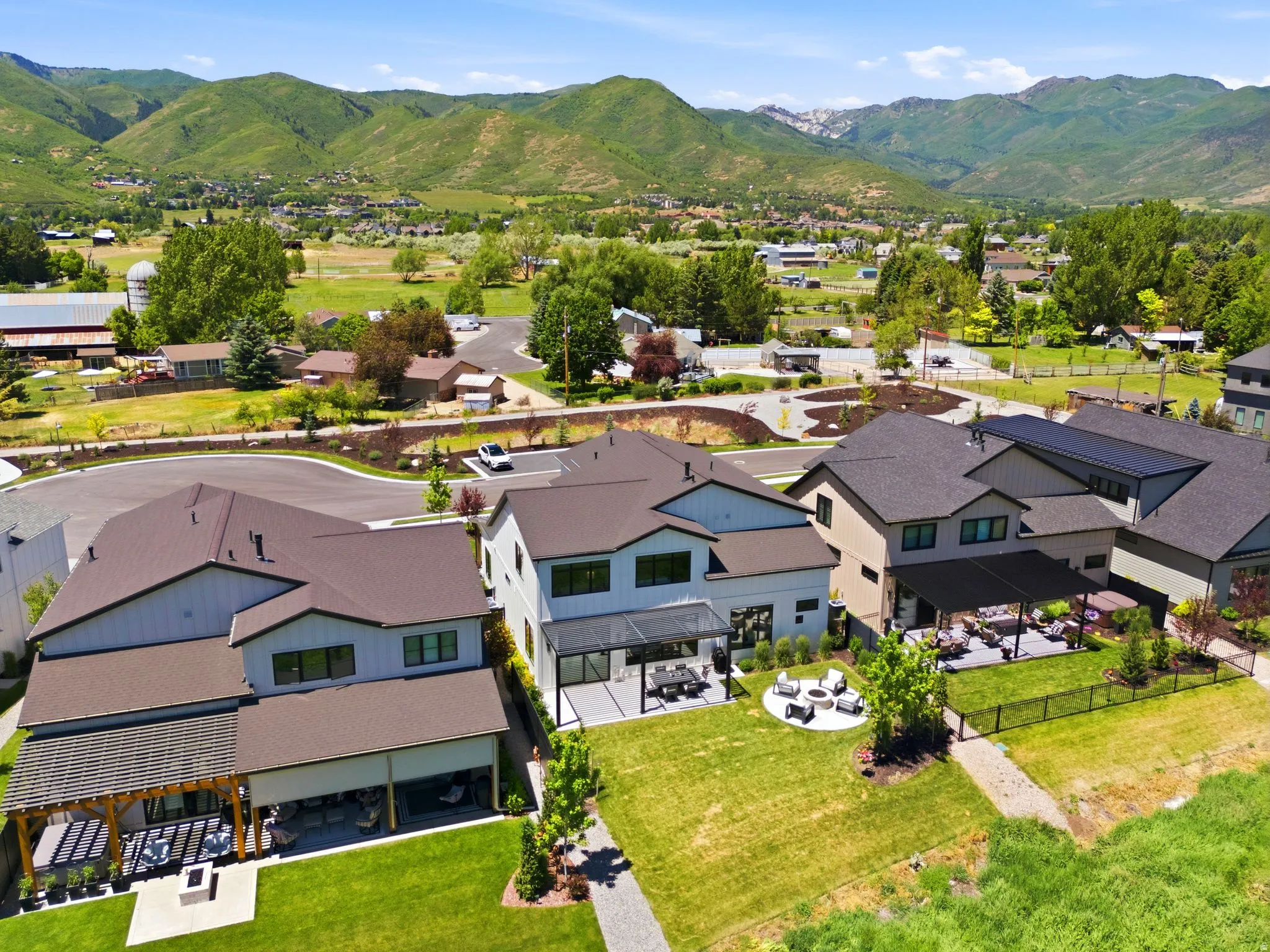 Modern residential property featuring a manicured lawn, covered patio, and a stone-paved fire pit area